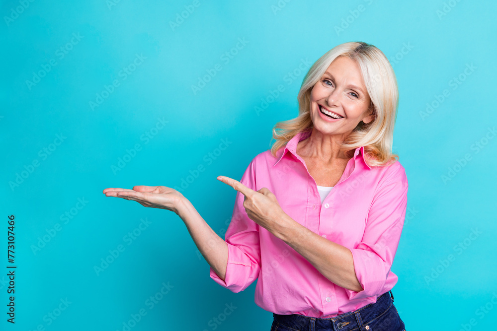 Photo portrait of pretty pensioner female point palm hold empty space wear trendy smart casual outfit isolated on cyan color background Photo portrait of pretty pensioner female point palm hold empty space wear trendy smart casual outfit isolated on cyan color background