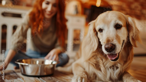 A golden retriever is eating from a bowl as a woman sits in the background.