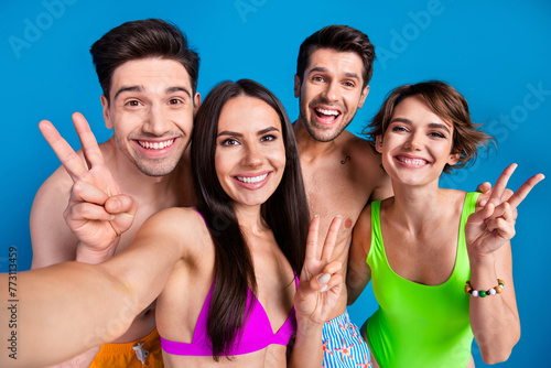 Photo of excited positive buddies company dressed bikini recording video vlog showing v-signs isolated blue color background