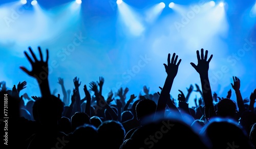 Silhouettes of a crowd with raised hands at a concert illuminated by stage lights. The concept of a live music performance.