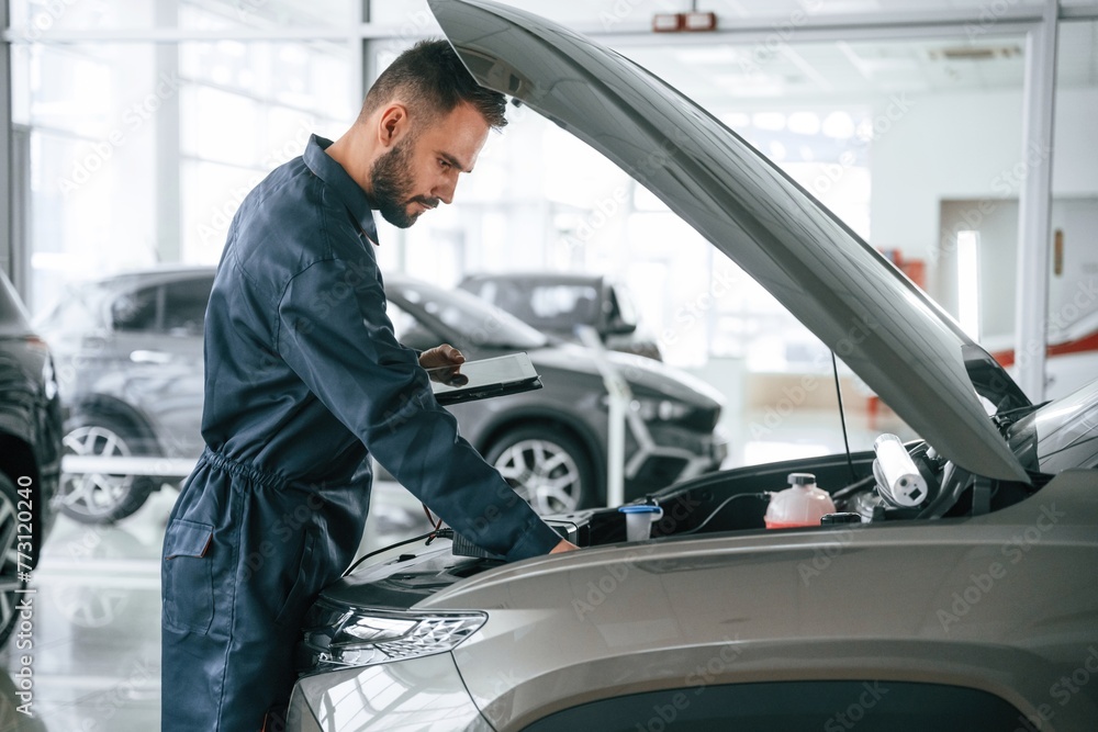 View from the side. Car repairman is in the garage with automobile View from the side. Car repairman is in the garage with automobile