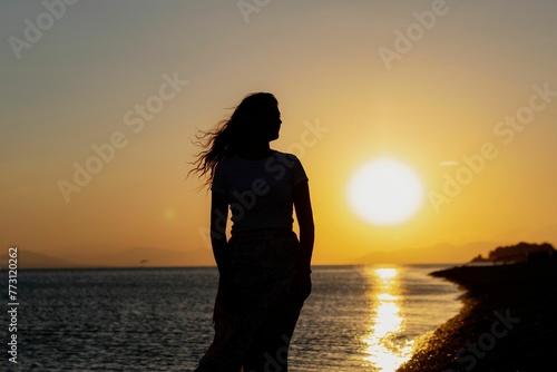 Beautiful silhouette of a female standing in the foreground of a stunning beach landscape at sunset © Wirestock