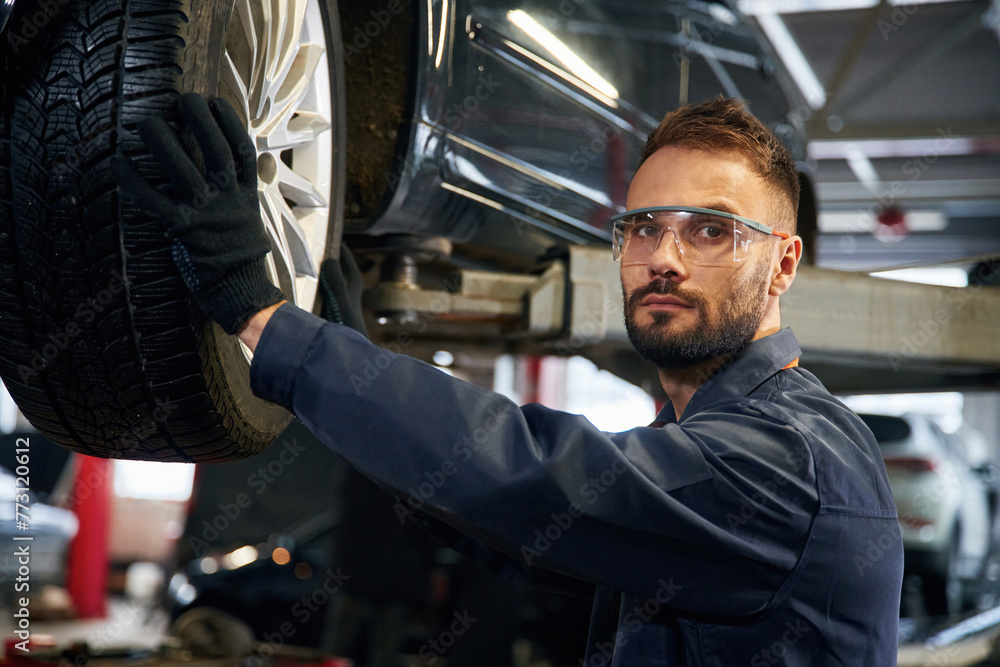 Looking at the camera. Car repairman is in the garage with automobile Looking at the camera. Car repairman is in the garage with automobile