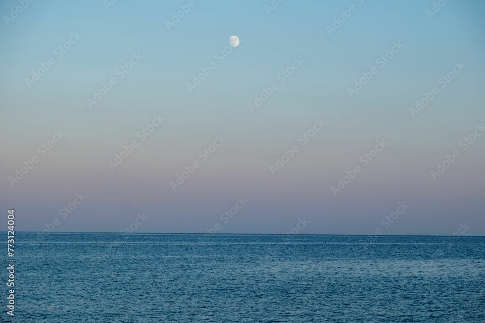 Scenic landscape of the ocean against a sunset sky with the moon in the background Scenic landscape of the ocean against a sunset sky with the moon in the background