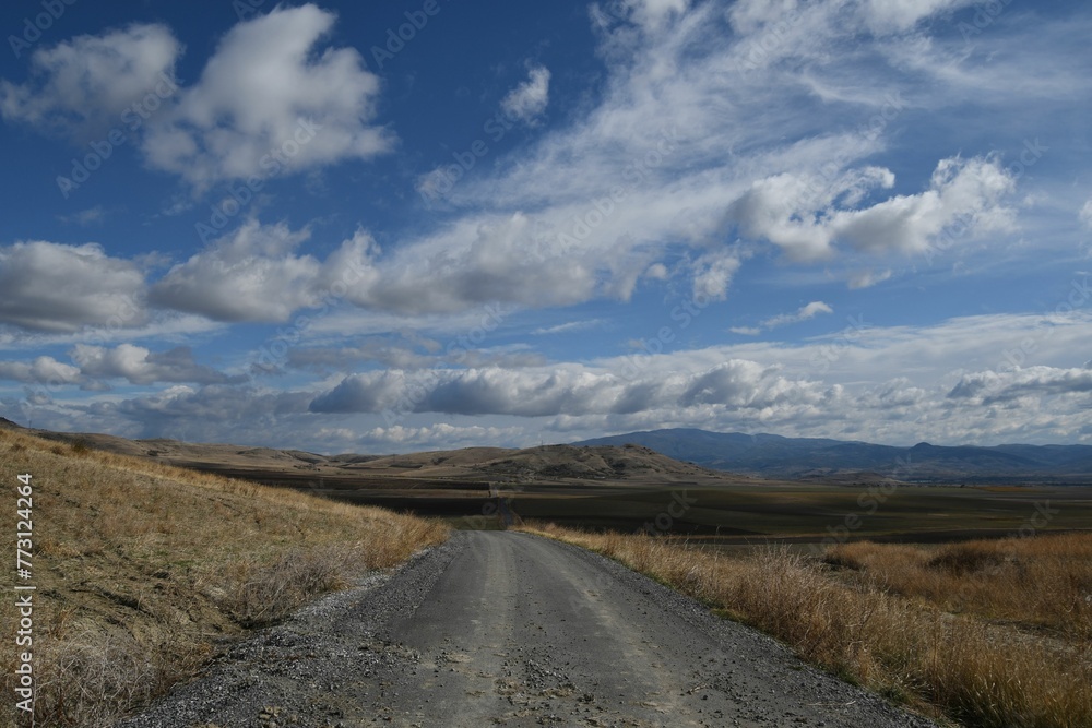 Scenic view of a dirt road leading through a lush landscape of grassy hills and mountains Scenic view of a dirt road leading through a lush landscape of grassy hills and mountains