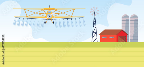 A plane sprays fertilizer on a field against the background of a farm, barn and wind turbine