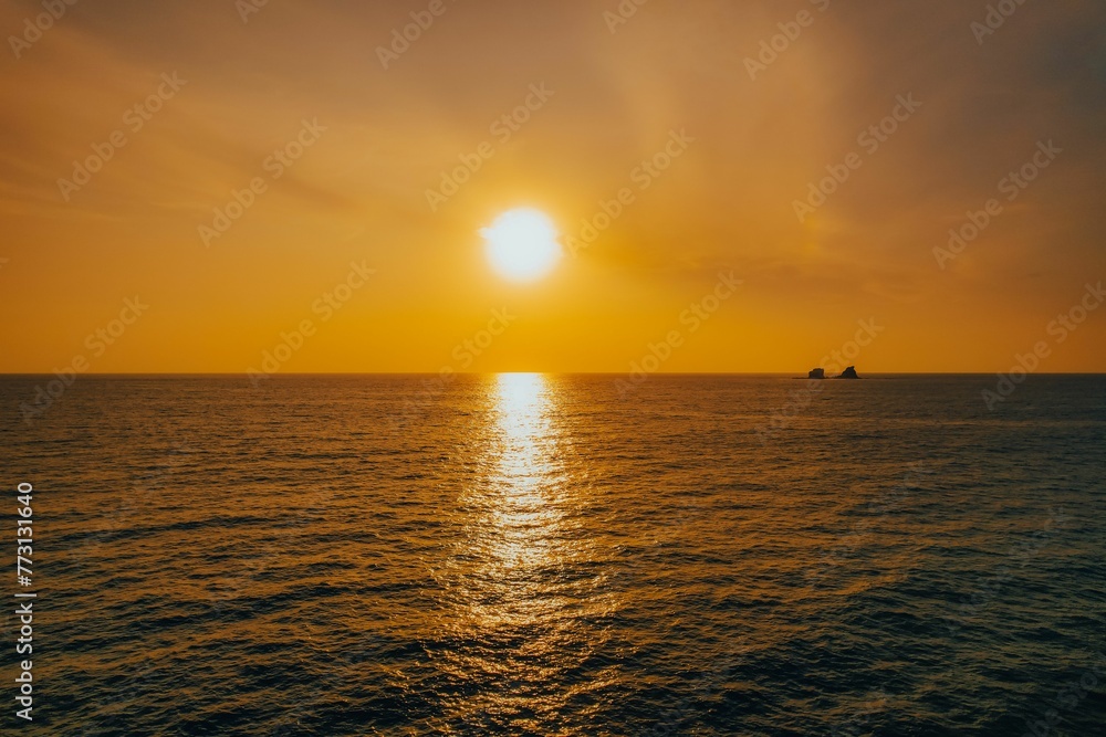 Majestic view of the sun setting over a serene ocean with a ship sailing in the background