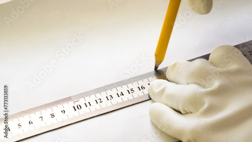 A male construction worker with a metal ruler and pencil draws a line in close-up. © woff