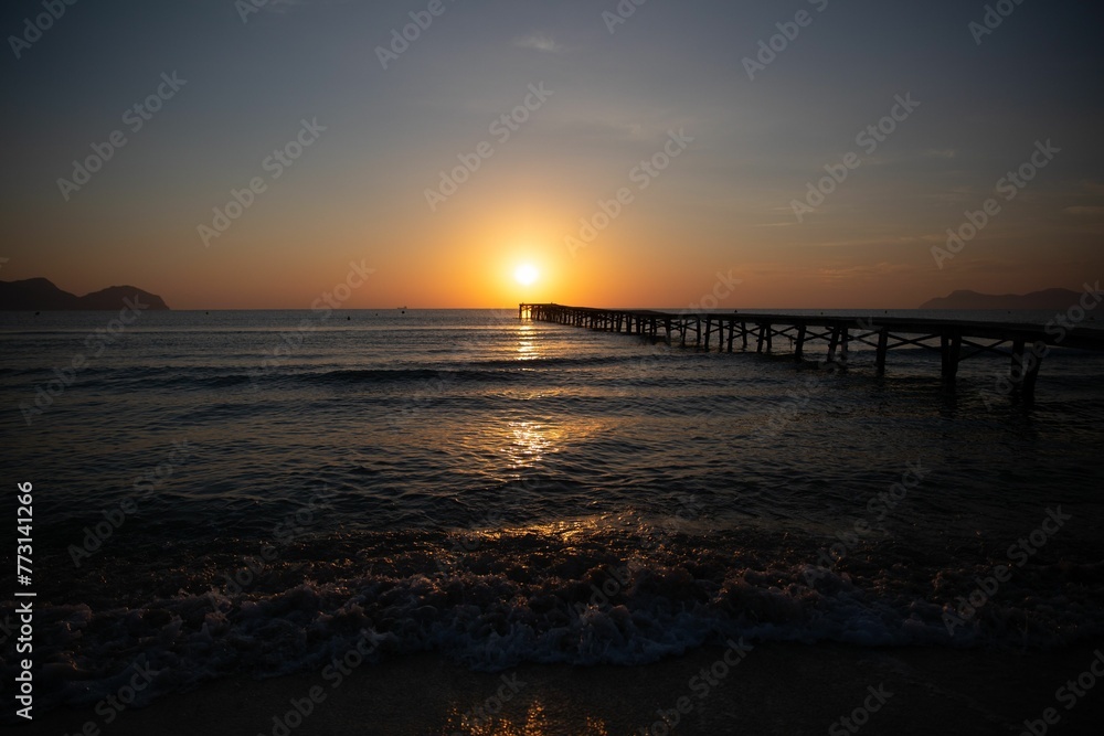 a sunset with a pier extending into the water near an island