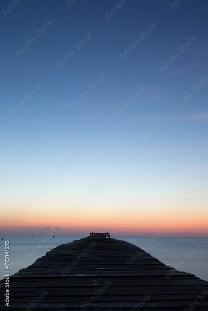 a long wooden dock stretches out into the ocean at dusk