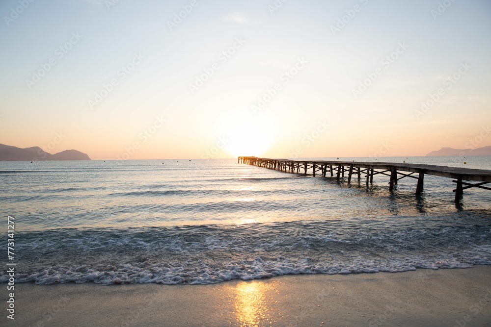 Fototapeta premium a sunset is shown with waves rolling in and a pier