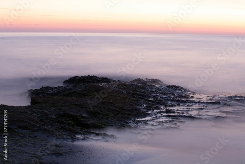 the sunset is lit over the water and rocks at the beach © Wirestock