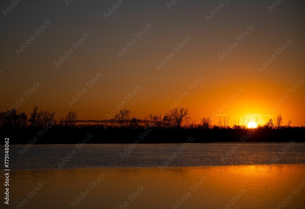 Breathtaking sunrise over a tranquil lake with silhouettes od trees.