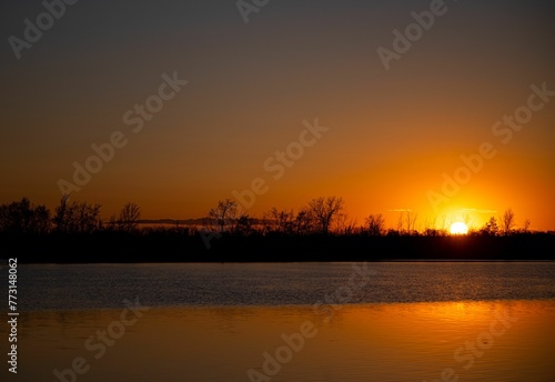 Breathtaking sunrise over a tranquil lake with silhouettes od trees.