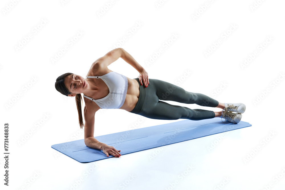 Dynamic portrait of young athlete woman stands in side plank and holds hand on hip against white studio background. Concept of sport and recreation, movement, self care, action, energy. Ad Dynamic portrait of young athlete woman stands in side plank and holds hand on hip against white studio background. Concept of sport and recreation, movement, self care, action, energy. Ad