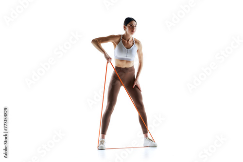 Muscular woman in workout pose with resistance band against white studio background, Strength and power. Concept of sport and recreation, movement, self care, action, energy. Ad