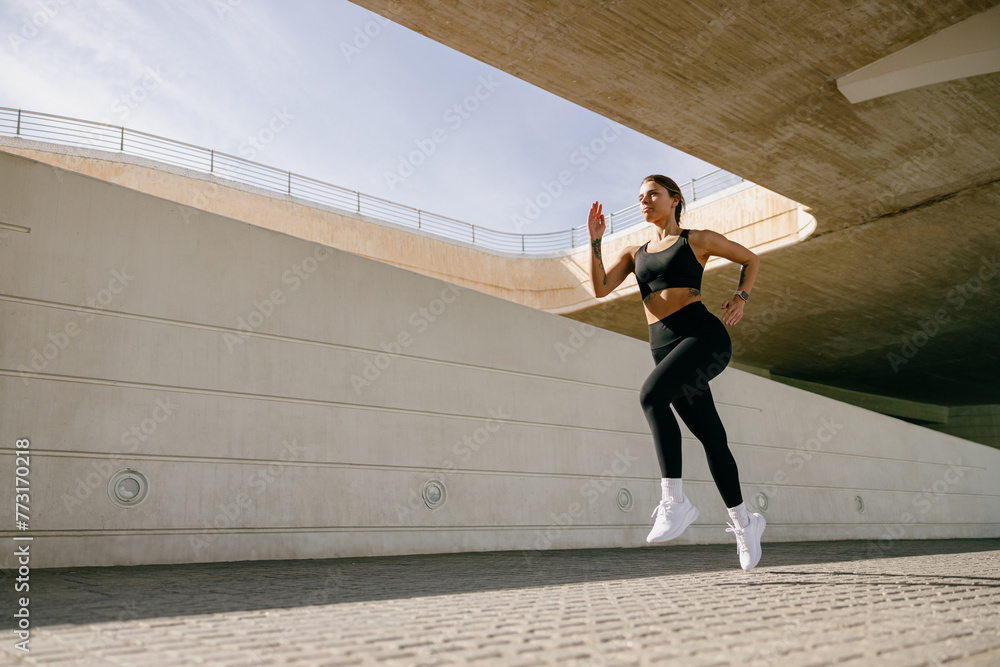 Naklejka premium Young woman in sportswear is running on modern buildings background. Active lifestyle concept