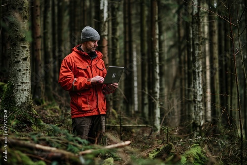 A man wearing a red jacket stands in a forest, using a laptop to analyze real-time data