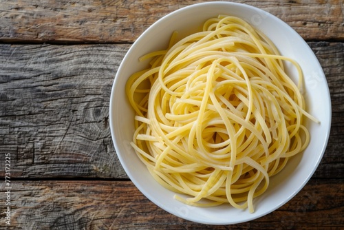 A close-up top-down view of a white bowl filled with artisanal handcrafted spaghetti on a wooden table