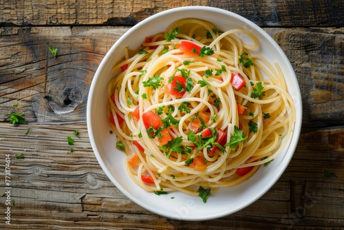 A white bowl filled with whole grain or vegetable-based spaghetti, mixed with a variety of colorful vegetables