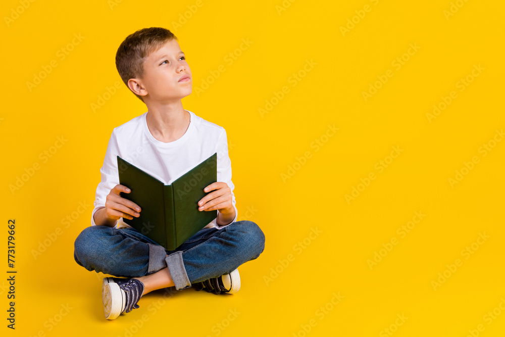 Full length photo of thoughtful dreamy kid dressed white shirt reading fairytale looking empty space isolated yellow color background Full length photo of thoughtful dreamy kid dressed white shirt reading fairytale looking empty space isolated yellow color background