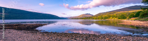 Large panorama au bord d'un loch avec plage de pierre et reflets des montagnes et des nuages dans l'eau en Ecosse l'été photo