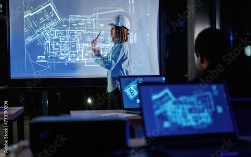In white hard hat. Female architect is showing construction site plan for building on projector