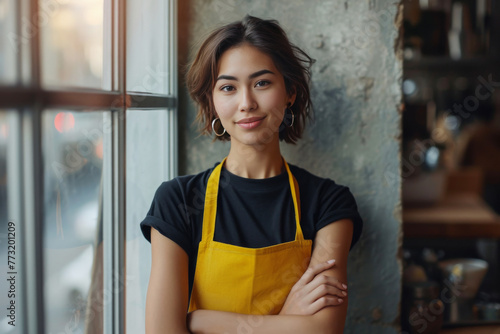 Young female entrepreneur with yellow apron and arms crossed in cozy cafe interior