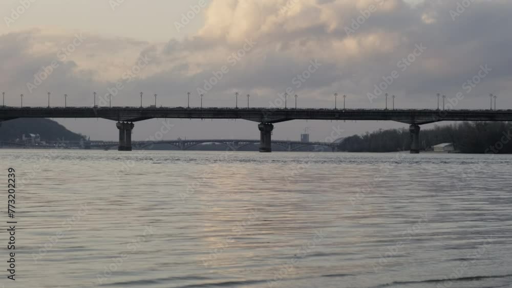 A girder bridge spans over a peaceful lake, with a cloudy sky in the background, creating a stunning natural landscape A girder bridge spans over a peaceful lake, with a cloudy sky in the background, creating a stunning natural landscape