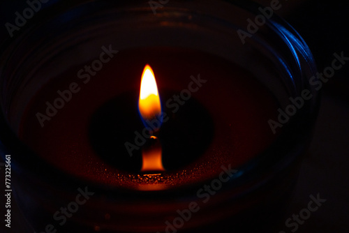Beautiful burning candle with the flame reflection on the melted wax Closeup. Oil lantern. Blue splash on dark black background. Minimalistic concept. Graphic design, poster. Copy text space. Bokeh.