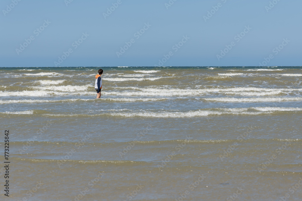 Jeune garçon habillé seul dans les vagues sur une plage de sable fin en Normandie