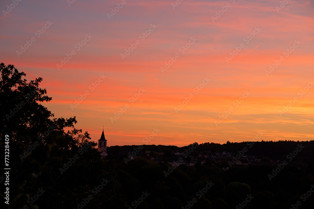 Silhouette of village and forest against sunset sky