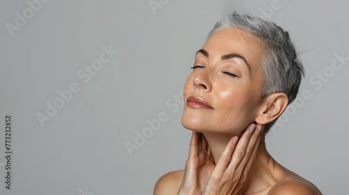 portrait of grey haired 60 year old woman softly touching her face and neck  concept of beauty at older age  senior  skincare rejuvenation  on grey background
