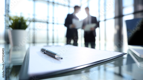 Two men are standing in front of a table with a pen and a piece of paper