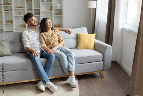 Canvas Print Relaxed hindu couple resting on sofa, chilling on comfy couch, cuddling and look