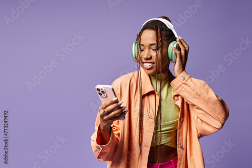 happy african american woman listening music in her headphones and using phone on lilac backdrop © LIGHTFIELD STUDIOS