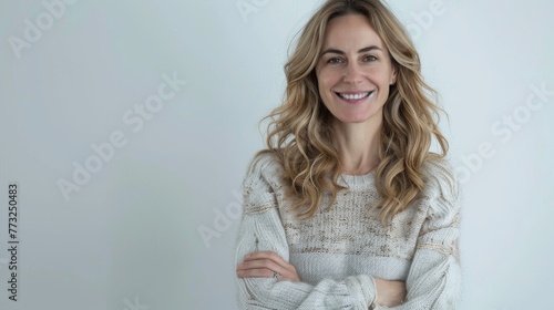 A young, ambitious and confident woman in her 30s faces the camera with crossed arms and a smile, looking forward, standing in front of a white background