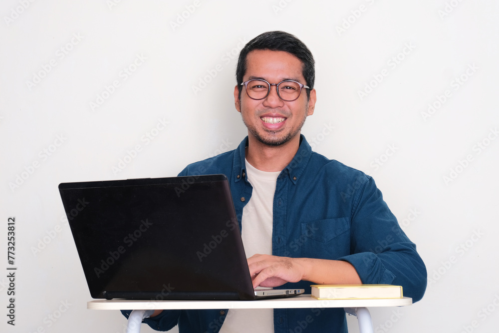 Adult Asian man smiling while working using a laptop Adult Asian man smiling while working using a laptop