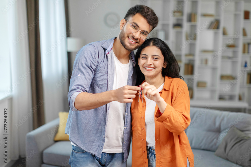 Satisfied young indian spouses show keys at own flat in living room, enjoy moving, buying new home, renting house together, copy space Satisfied young indian spouses show keys at own flat in living room, enjoy moving, buying new home, renting house together, copy space