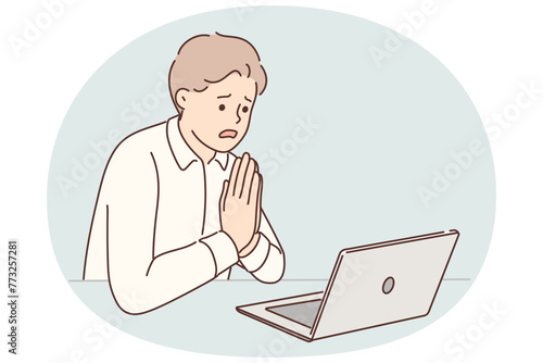 Man manager prays sitting at table with laptop asking god for help after making mistakes in project