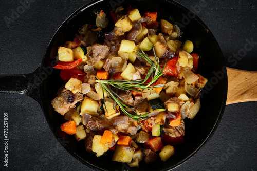 Top view of a hearty skillet beef ragout with mixed vegetables on a textured black backdrop