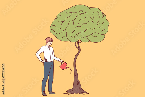 Businessman develops own intelligence by watering trees with brain shaped leaves as metaphor for receiving business education. Guy entrepreneur cares about gaining new knowledge and developing brain