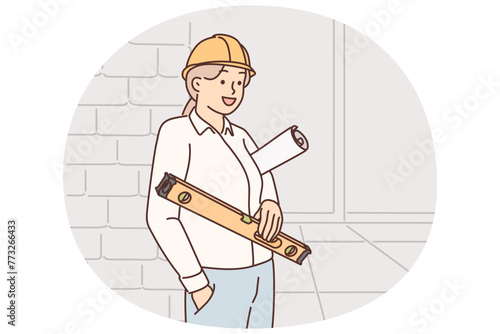 Woman architect stands in building under construction with level and folded blueprints in hands