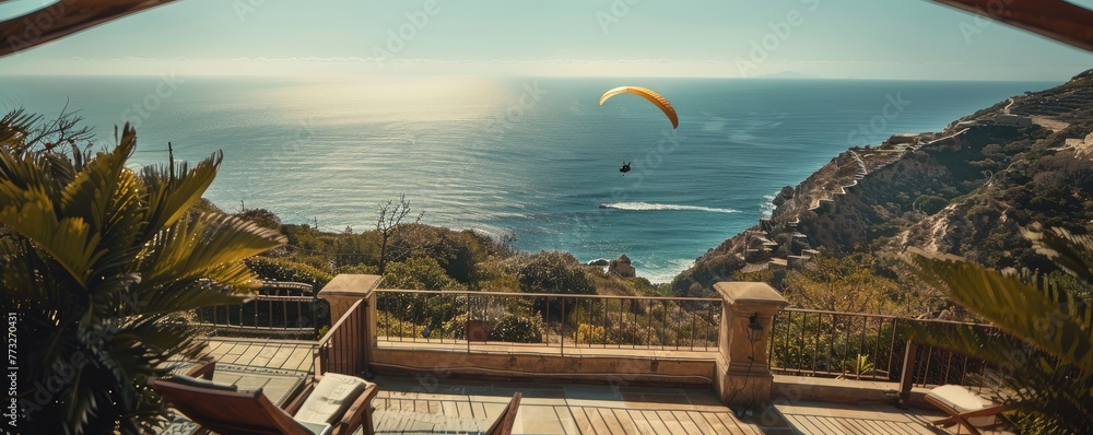 Modern cliffside villa overlooks the ocean with a paraglider soaring by, signifying luxury living and adventure.