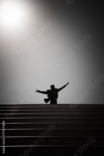 Silhouette of a man standing on the stairs and raising his hands. Statue of Domenico Modugno. Polignano a Mare, Italy