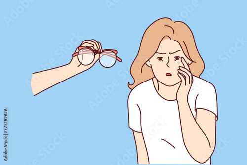 Blind woman with poor vision looks closely at small text on computer screen, standing near hand with glasses. Blind girl refusing eyeglasses, compelled to squint during test at ophthalmologist