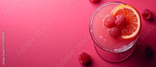  A tight shot of a glass containing a drink against a pink backdrop, garnished with a few plump raspberries