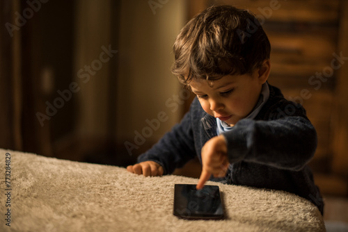 Baby one year old boy touching smartphone at home living room.