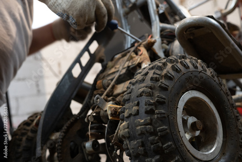 An ATV being repaired by an unqualified mechanic in a garage. A mechanic tightens a part on an ATV using a ratchet screwdriver. Replacing parts on a small ATV in your garage.