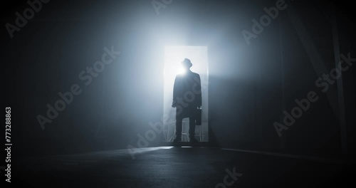Silhouette of a man dressed in long coat with hat walking to a dark room through a door. Cinematic shot. High quality 4k footage photo